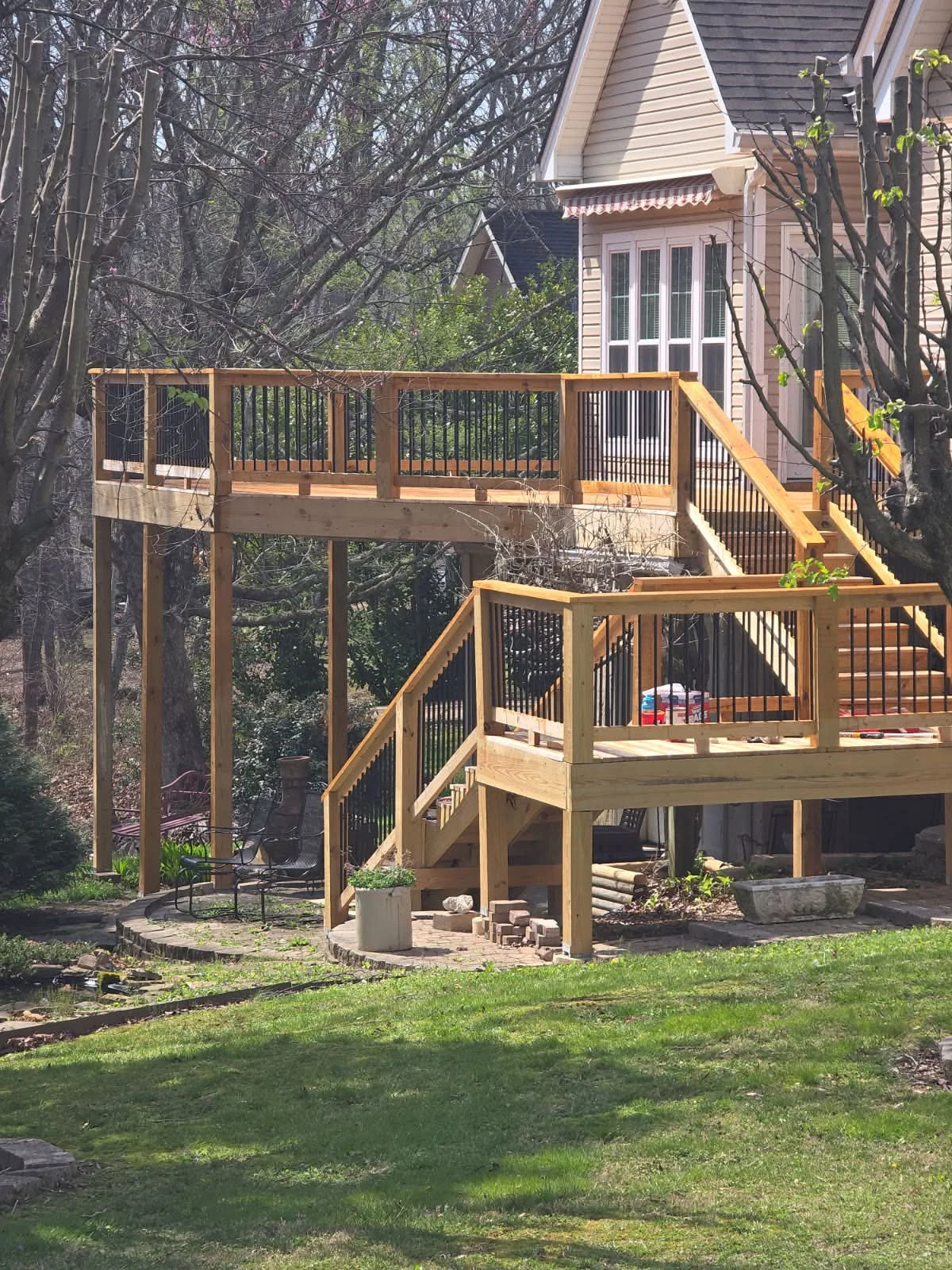 Multilevel wooden deck with black balusters and stairs beside a home